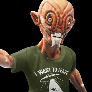 May include: A green t-shirt with a white graphic of a UFO and the text "I WANT TO LEAVE". The graphic shows a person falling from the UFO into a forest.