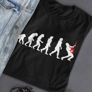 May include: Black t-shirt featuring a white graphic of the evolution of man, culminating in a person playing a red electric guitar.