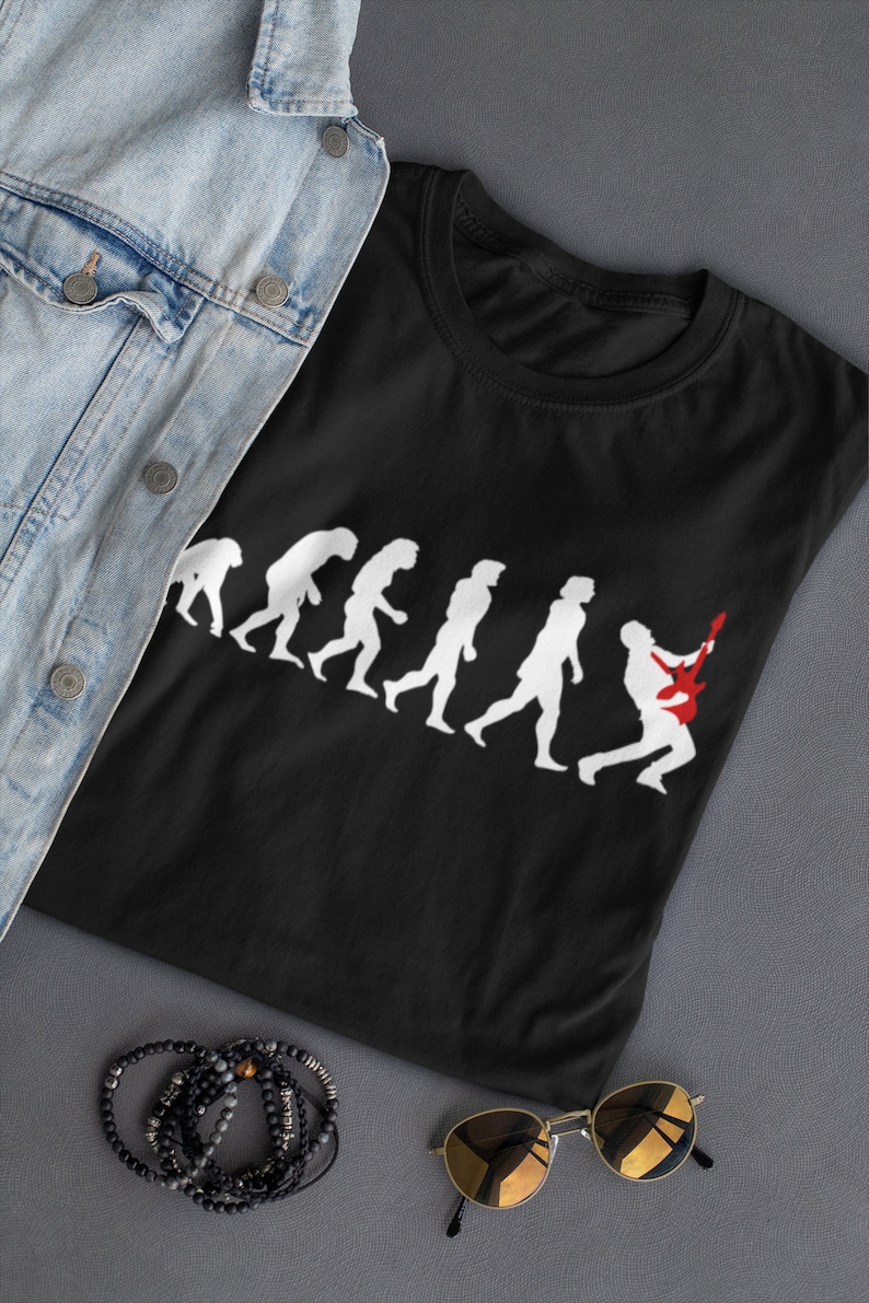 May include: Black t-shirt featuring a white graphic of the evolution of man, culminating in a person playing a red electric guitar.