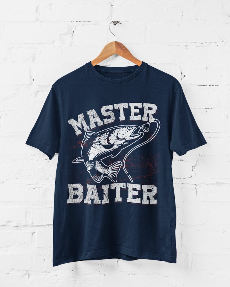 May include: A navy blue short-sleeve t-shirt featuring a white graphic of a fish on a fishing line. The text "MASTER BAITER" is printed in a distressed white font above and below the fish illustration, centered on the front of the garment.