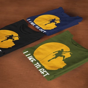 May include: Three folded t-shirts with a graphic of a person rock climbing on a yellow sun. The text on the shirts reads "I like to get high". The shirts are black, navy blue, and army green.