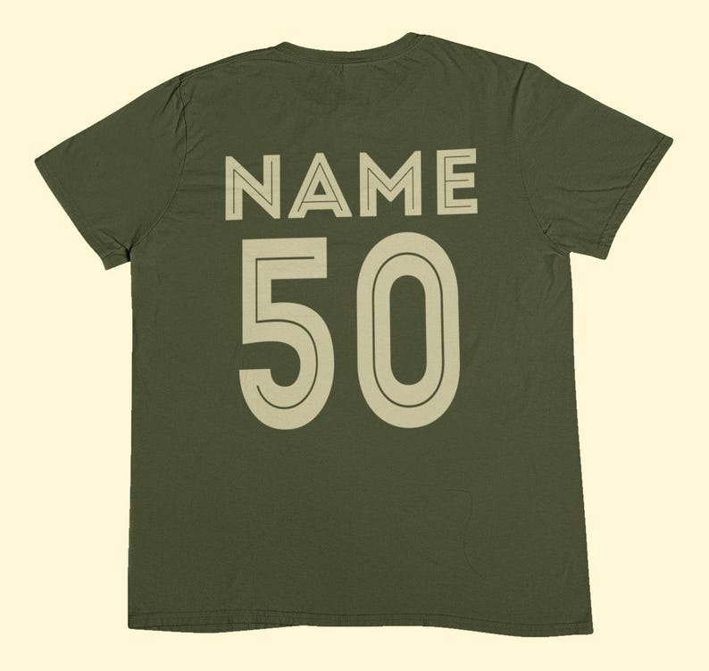 May include: An olive green short-sleeve t-shirt featuring the word NAME printed in a light beige sans-serif font above the number 50 in a matching light beige font. The design is centered on the back of the garment with a clean, bold aesthetic.