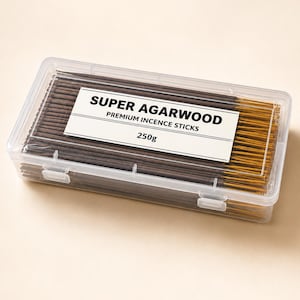 May include: A clear rectangular plastic container filled with dark brown incense sticks. A white label on the lid features the black text SUPER AGARWOOD, PREMIUM INCENCE STICKS, and 250g. The sticks have visible wooden ends inside the transparent box.
