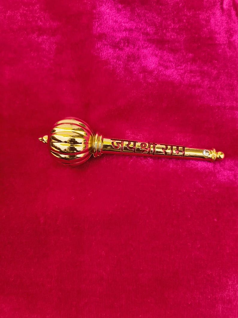 Op de afbeelding: Een gouden metalen knots met een ronde kop en een lange steel. De steel is gegraveerd met de tekst "जय श्री राम".