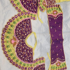 May include: Three pieces of yellow and purple fabric with intricate embroidery and embellishments. The fabric is decorated with floral patterns, swirls, and sequins.