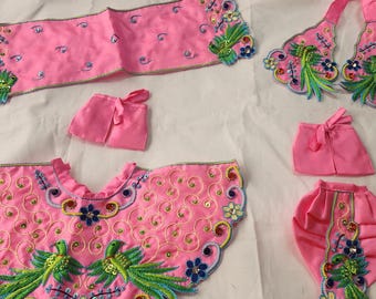 May include: A pink baby outfit with embroidered birds and floral designs. The outfit includes a cape, a top, a skirt, a diaper cover, and a headband.