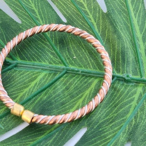 May include: A copper and silver twisted wire bangle bracelet. The bracelet is open and has a small gold bead at the end.
