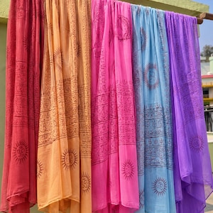 Può includere: Una collezione di cinque sciarpe leggere in rosso, arancione, rosa, azzurro e viola. Ogni sciarpa presenta una stampa ripetuta color marrone scuro di simboli solari e complessi motivi geometrici disposti in fasce verticali sul tessuto.