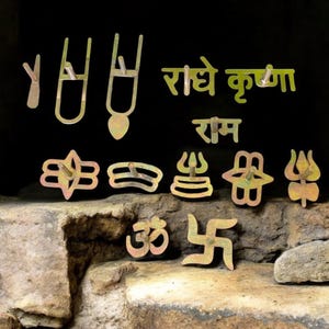 May include: A collection of gold-colored metal religious symbols and text against a black background. The symbols include a trident, a lotus flower, and the Om symbol. The text is in a foreign language.