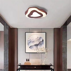 May include: A modern ceiling light fixture with a unique, organic shape. The light features a brown, white, and dark brown color scheme. The fixture is mounted on a white ceiling, and the room has a minimalist design.