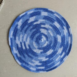 Puede incluir: Una alfombra redonda de crochet azul y blanco con un patrón circular. La alfombra está hecha de hilo y tiene una superficie suave y texturizada.