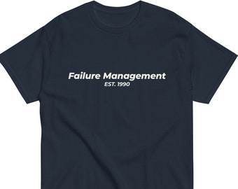 以下が含まれることがあります： 白文字で「Failure Management」と「EST. 1990」と書かれたネイビーブルーのTシャツ。半袖シャツは柔らかい素材で作られています。テキストはシャツの前面の中央に配置されています。