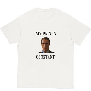 Puede incluir: Camiseta blanca con el texto "MY PAIN IS CONSTANT" en negro, sobre y debajo de un retrato de un hombre con traje. La camiseta tiene cuello redondo y mangas cortas.