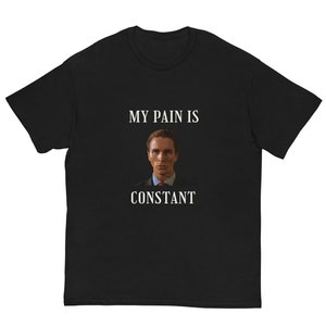 Puede incluir: Camiseta negra con el texto blanco "MY PAIN IS CONSTANT". La camiseta presenta un retrato de un hombre con traje y corbata. La camiseta es de estilo cuello redondo clásico.