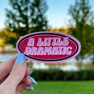 May include: A pink and black oval sticker with the text "A little dramatic" in a retro font. The sticker has a pink background with black outlines and white stars.
