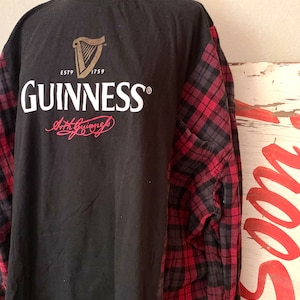 May include: Black t-shirt with a red and black checked long-sleeved shirt layered over it. The t-shirt has the Guinness logo and the text "ESTD 1759 GUINNESS" printed on the back.