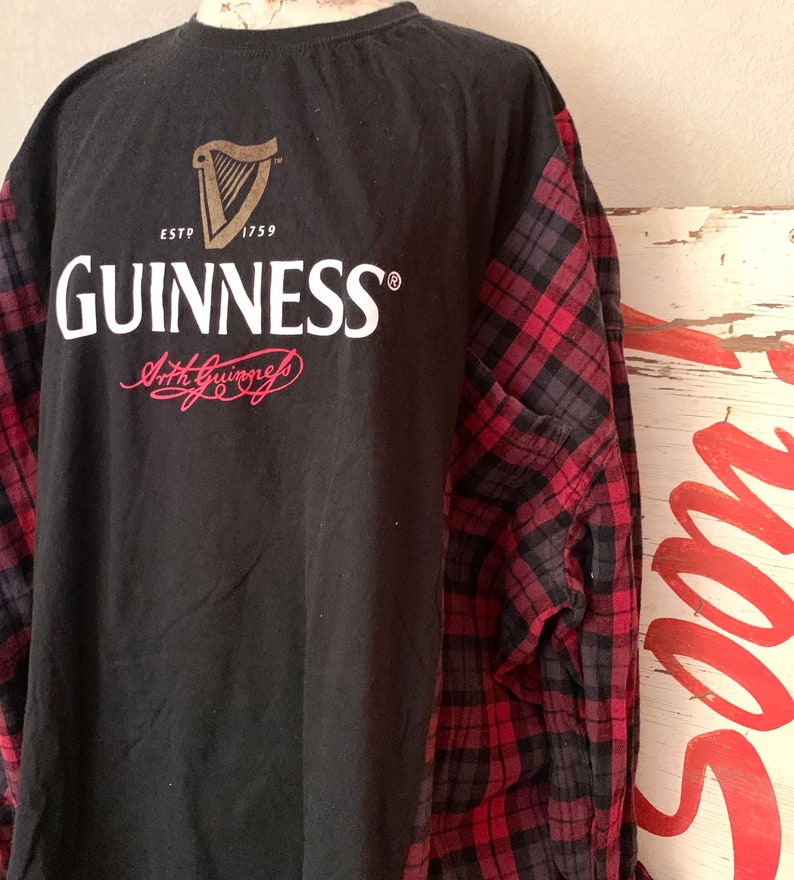 May include: Black t-shirt with a red and black checked long-sleeved shirt layered over it. The t-shirt has the Guinness logo and the text "ESTD 1759 GUINNESS" printed on the back.
