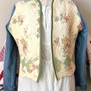 May include: A quilted jacket with a floral print and denim sleeves. The jacket has a green trim and is open in the front.