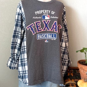 Puede incluir: Camiseta gris de manga larga con una camisa de cuadros azules y blancos superpuesta. La camiseta tiene un estampado gr&aacute;fico que dice "Property of MLB Authentic Collection Texas Baseball".