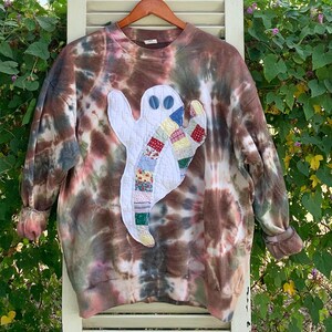 May include: A brown, blue, and white tie-dye sweatshirt with a patchwork ghost appliqué. The ghost is made of various colorful fabrics and has two black eyes.