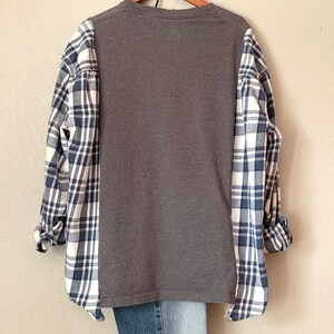 Puede incluir: Una camisa gris de manga larga con un patr&oacute;n de cuadros en las mangas. La camisa tiene un corte holgado y un cuello redondo.