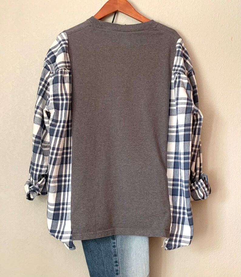 Puede incluir: Una camisa gris de manga larga con un patr&oacute;n de cuadros en las mangas. La camisa tiene un corte holgado y un cuello redondo.