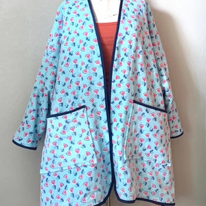 May include: A light blue long-sleeved robe with a watermelon print and navy blue trim. The robe has two patch pockets on the front.