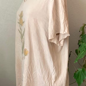 Puede incluir: Una camiseta de color rosa p&aacute;lido de gran tama&ntilde;o con un dise&ntilde;o floral impreso en la parte delantera. El dise&ntilde;o presenta flores amarillas y hojas verdes.