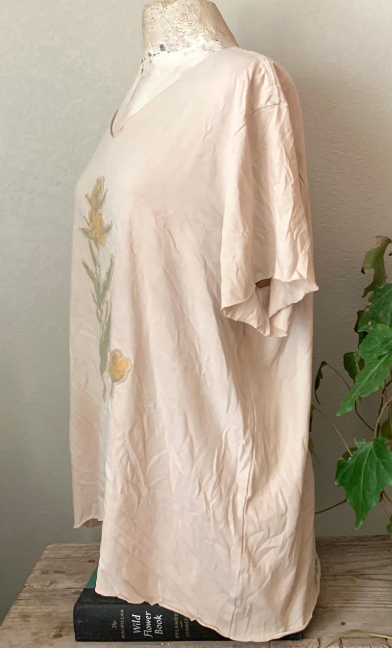 Puede incluir: Una camiseta de color rosa p&aacute;lido de gran tama&ntilde;o con un dise&ntilde;o floral impreso en la parte delantera. El dise&ntilde;o presenta flores amarillas y hojas verdes.