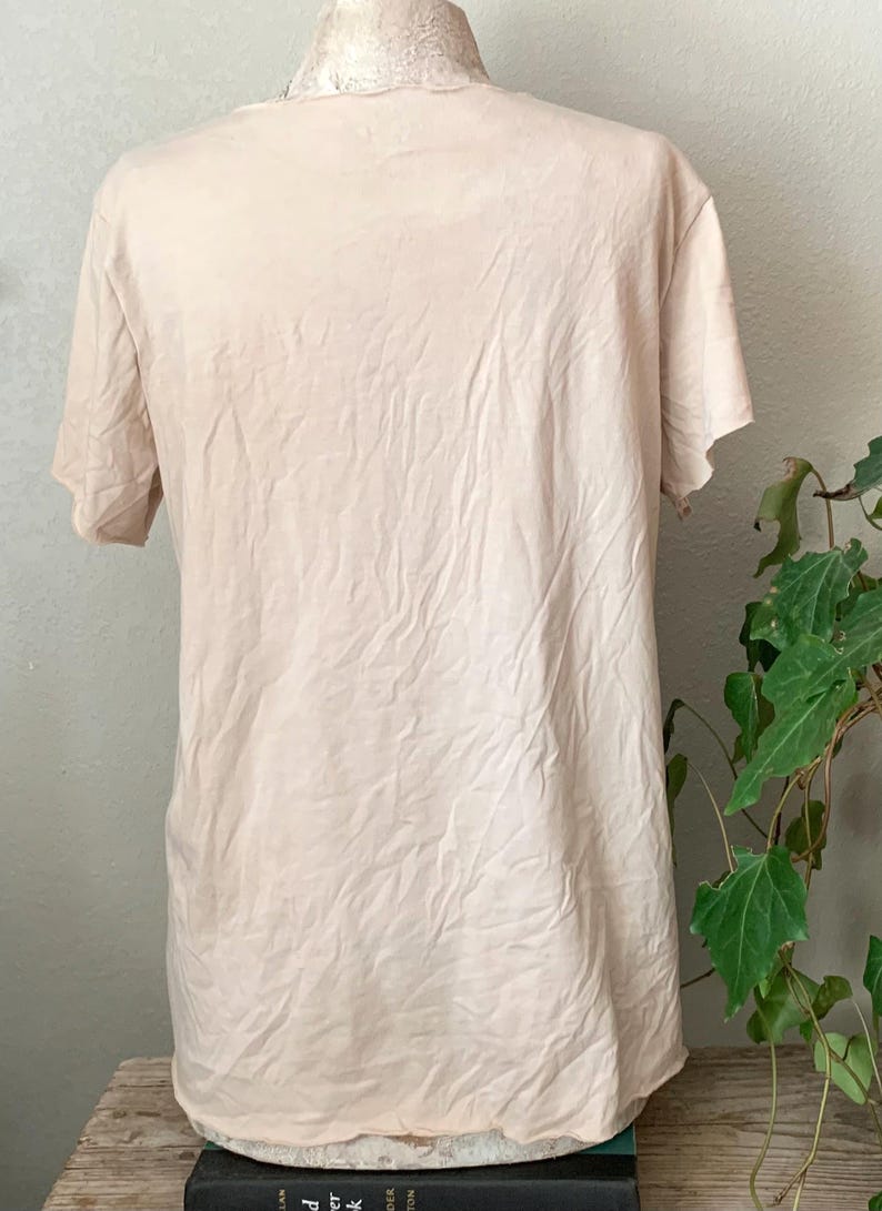 Puede incluir: Una camiseta de color beige claro con un escote ligeramente desgastado. La camiseta est&aacute; hecha de una tela suave y texturizada.