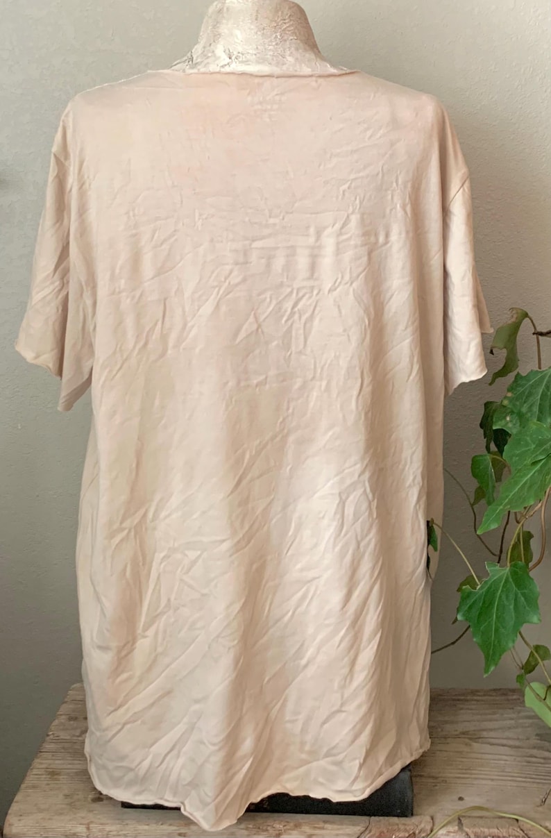 Puede incluir: Una camiseta lisa de color blanco roto, de manga corta, con una textura ligeramente arrugada. La camiseta est&aacute; hecha de una tela suave y ligera.