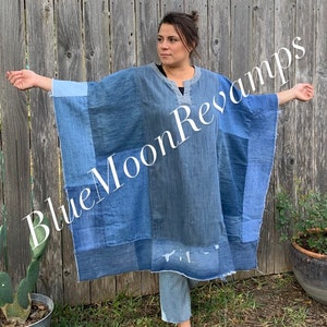 May include: A blue denim poncho made from repurposed denim fabric. The poncho has a patchwork design with different shades of blue denim. The poncho is worn by a person standing in front of a wooden fence.