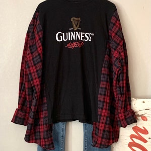 May include: A black t-shirt with a red and black checked shirt layered over it. The t-shirt features a Guinness logo with the text "ESTD 1778 GUINNESS" and a signature.