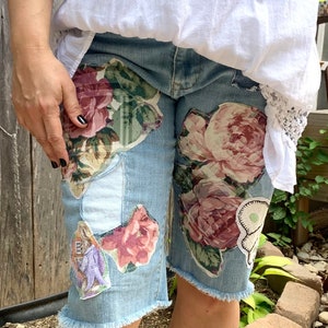 May include: Light blue denim shorts with floral fabric patches sewn on. The patches are in shades of pink, green, and white.