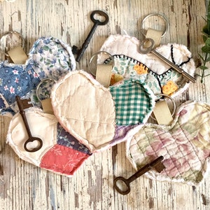 May include: A set of six patchwork heart-shaped keychains with antique keys attached. Each keychain is made of different fabrics in shades of pink, blue, green, and white.