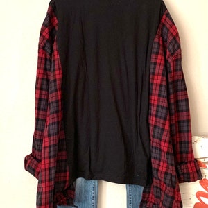 May include: A black long-sleeved shirt with red and black plaid flannel sleeves. The shirt is worn over blue jeans.