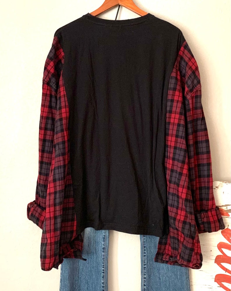 May include: A black long-sleeved shirt with red and black plaid flannel sleeves. The shirt is worn over blue jeans.