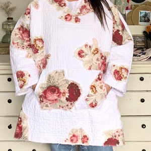 May include: White quilted jacket with a floral print. The jacket has a V-neck and long sleeves. The floral print is in shades of pink, red, and green.