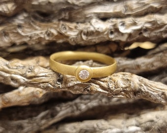 May include: A simple gold band ring with a single, small, clear diamond set in the center.