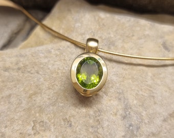 May include: A gold pendant with a green oval gemstone set in a bezel setting. The pendant is on a gold chain.