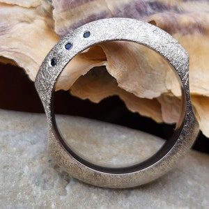 May include: A silver ring with a textured finish and four small blue gemstones set in the band.