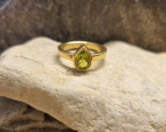 May include: A gold ring with a pear-shaped green gemstone set in the centre.