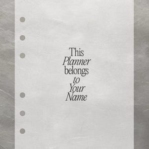 May include: A white planner page with six pre-punched holes. The text "This Planner belongs to Your Name" is printed in a serif font. The page is set against a textured, silver-grey background.
