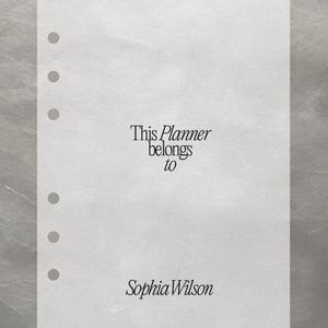 May include: A white planner page with pre-punched holes. The text "This Planner belongs to Sophia Wilson" is printed in a serif font. The background is a textured, silvery-gray.