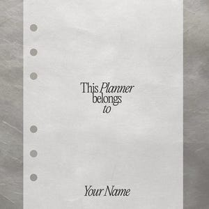 Può includere: Una pagina bianca di pianificatore con sei fori preforati. Il testo "This Planner belongs to Your Name" è stampato in un carattere serif. Lo sfondo è una superficie strutturata, grigio chiaro.