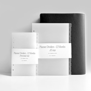 Könnte beinhalten: Eine Sammlung von Planer-Zubehör, darunter weiße Trennwände mit der Aufschrift "Planner Dividers - 12 Months" in den Größen Personal und A5, sowie ein schwarzer Planer-Einband mit Lederstruktur. Die Trennwände haben nummerierte Register.