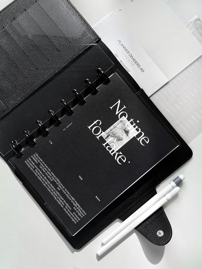 May include: Black planner dividers with the text "PLANNER DIVIDERS A5" and "MY ROADMAP" on the top. The dividers are in a black leather planner with a clear plastic sheet with the text "No time for fake" and "TOO BUSY".