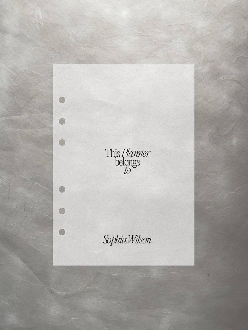 May include: A white planner page with pre-punched holes. The text "This Planner belongs to Sophia Wilson" is printed in a serif font. The background is a textured, silvery-gray.