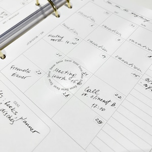 May include: A close-up of a white planner with a gold binder. The planner has a weekly layout with dates and days of the week. There are several handwritten appointments and notes, including "Meeting Work 15:20", "Call w. Client B. 17:20", and "Friends Dinner".