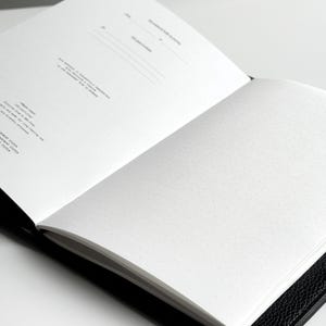 K&ouml;nnte beinhalten: Ein offenes schwarzes Notizbuch mit wei&szlig;en Punktrasterseiten. Die linke Seite hat Linien f&uuml;r das Datum und andere Informationen. Die rechte Seite ist leer mit einem Punktrastermuster.